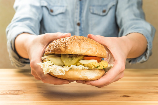 Vegetarian burger in hands. Close-up image of vegetarian hamburger sandwich in female hands above wood kitchen table