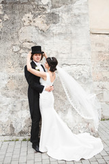 Beautiful bride hugs tall groom in black tuxedo and topper