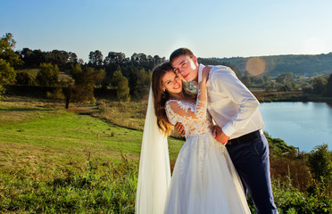 Bride and groom looking at the camera in the sunny summer day near lake. Beauty sunlight at the outdoor in happy wedding day