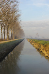 Canal in the countryside near a gravel road and a row of trees