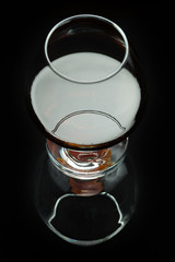 A glass of cognac on a black background with reflection, top view