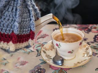 Tea being poured form a vintage tea pot, cosy or cozy and tea cup.