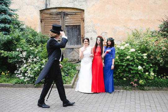 Man in tailcoat and topper passes bride and bridesmaids standing on the road