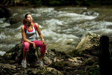 Young woman hiker rests next to the forest river