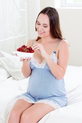 Happy pregnant woman sitting on the bed. A young pregnant woman is sitting in the bedroom. Pregnant woman relaxing. Young pregna