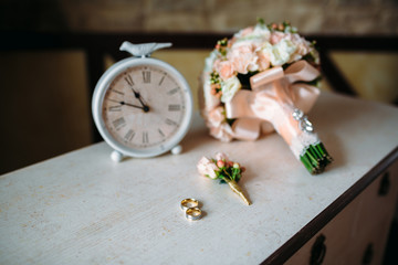 Wedding accessories. Boutonniere, Golden rings, a beautiful bouquet of flowers on white textured table. Concept of bride and groom ornamentation