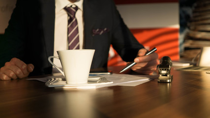 Fototapeta na wymiar Kaffeetasse steht auf einem Schreibtisch während ein Unternehmer Verkaufszahlen prüft