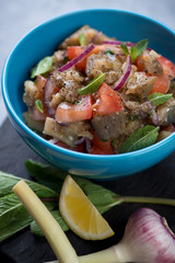 Salad with baked aubergines, fresh red tomatoes and mint served in a blue ceramic bowl, close-up
