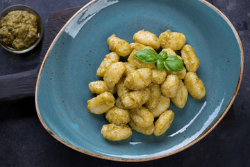 Potato gnocchi served with basil pesto sauce in a turquoise plate, top view, close-up