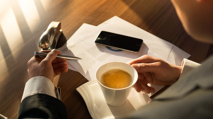 Junger Mann sitzt am Schreibtisch und trinkt Kaffee während er ein Dokument prüft
