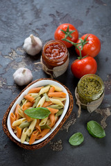 Three-colored penne pasta with two types of pesto sauces on a dark brown stone background, studio shot
