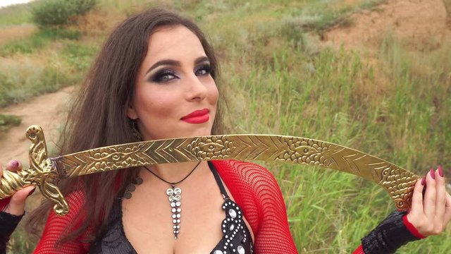 Oriental Beauty dance with a sword. Tribal style. Nice girl in national dress dancing in the open air. Nomads. Close-up portrait