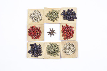 Several peppers, juniper and star anise on small wooden square bowls
