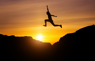 Silhouette of athlete, jumping over rocks in mountain area against sunset. Training running and jumping in difficult conditions in a beautiful nature with cloudy sky