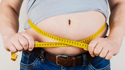 The belly of a fat man isolated on white background. Fat man holding a measuring tape. Weight Loss.