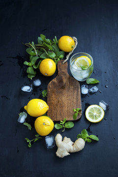 Wooden board with lemons, mint leaves, ginger, ice cubes and mineral water.Lemonade or mojito ingredients