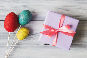 Gift box and painted Easter eggs over wooden background