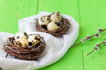 Easter quail eggs in nests.  Green wooden table. Pussy-willow in a vase