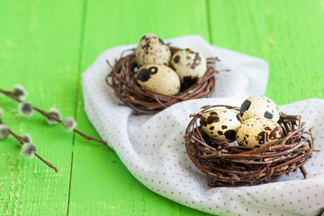 Easter quail eggs in nests.  Green wooden table. Pussy-willow in a vase