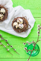 Easter quail eggs in nests.  Green wooden table. Pussy-willow in a vase