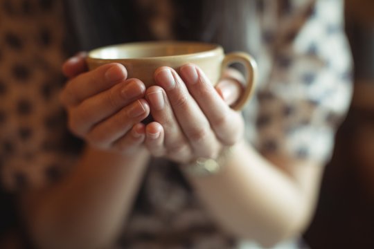 Mid section of woman holding a cup of coffee in hand