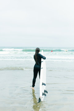 20-something female walks into ocean to surf in San Francisco, California