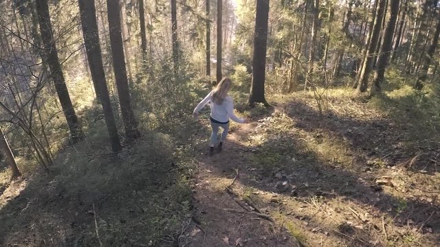 Blonde woman walks not careful through the sunny woods and then it suddenly slips. Slow motion.
