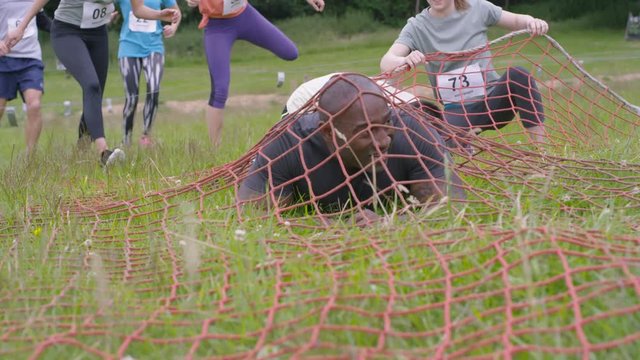  Competitors in assault course race running & crawling under net on the ground. 