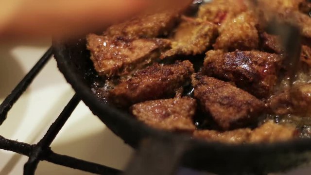 Pieces of liver in oil are fried in a frying pan in a home kitchen