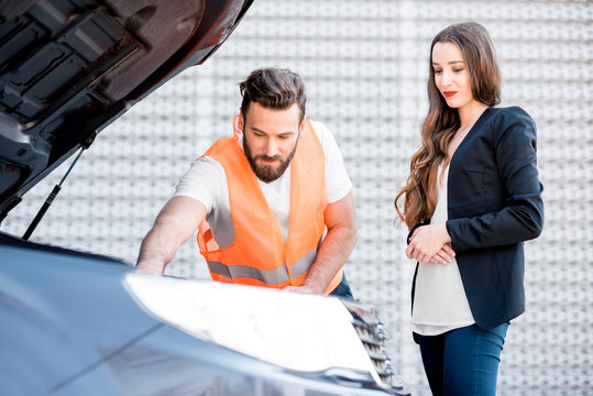Handsome service worker consulting or providing technical assistance of the broken car to the businesswoman standing near the service center building