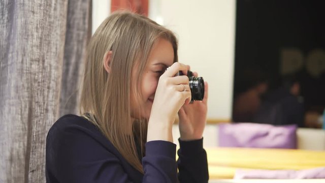 Young girl taking photos with vintage camera in cafe, having fun. Shot in 4k
