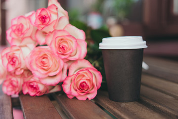 Take away coffee and  bouquet of pink roses on wooden background. Street coffee