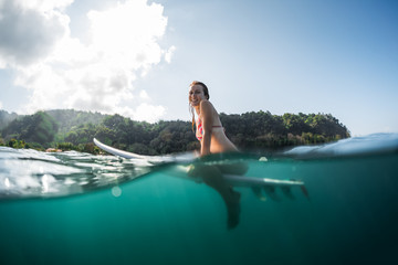 Woman smiles and sits on the surfboard in the ocean. Splitted shot with underwater view