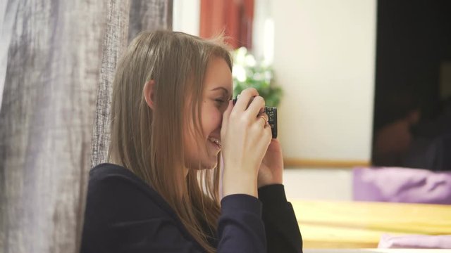 Young girl taking photos with vintage camera in cafe, having fun. Shot in 4k