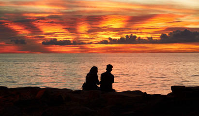 Silhouettes of a young man and a girl sitting on the beach at sunset time