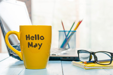 Hello MAY - text on yellow coffee cup at business office background, workplace with laptop and glasses. Spring time, empty space for text © bychykhin