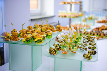 Beautifully decorated catering banquet table with burgers and profiteroles. Variety of tasty delicious snacks on the table