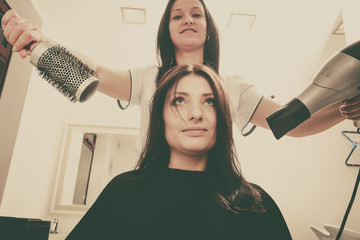 Hairdresser drying dark female hair using professional hairdryer