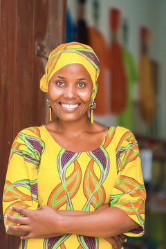 Young African woman in traditional clothes standing in entrance of her store, smiling at camera