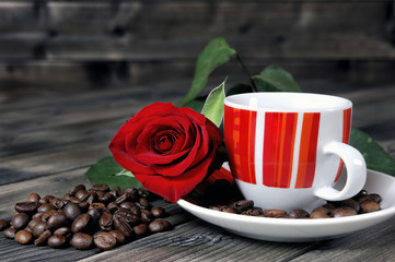View of a coffee cup on a wooden table old adorned with a red rose and coffee beans.