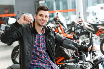 Cheerful owner. Shot of a stunning handsome young man sitting on his new motorbike holding keys...