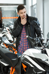 Expensive toy. Vertical portrait of a young handsome man checking out a motorbike rubbing his chin at the local motorcycle salon
