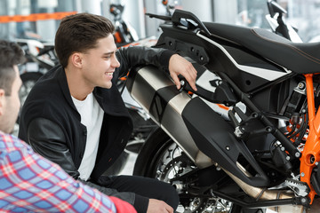 Fototapeta na wymiar I love this one. Shot of a stunning hot handsome young man laughing cheerfully looking at the new motorbike while listening to motorcycle salon manager speaking