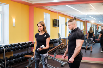 Woman with her personal fitness trainer in the gym exercising power gymnastics with a barbell