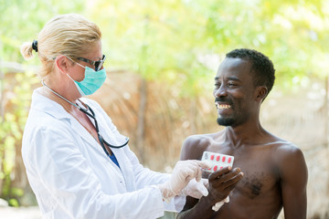Smiling African black man taking pills from the Caucasian female doctor outdoors