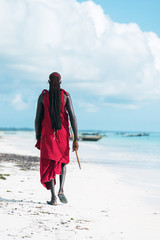 Rear view of walking Masai man on the white sand beach
