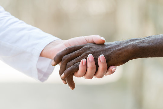 Helping hands.Caucasian doctor woman's hand holding black African man's hand.Unrecognizable people