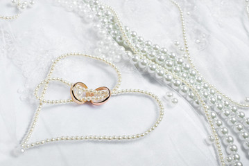 Gold wedding rings lie on a wedding dress. Against the background of the necklace of pearls 