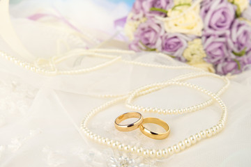 Gold wedding rings lie on a wedding dress. Against the background of the necklace of pearls 