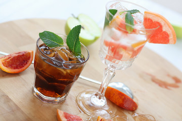 Two cocktails of whiskey with cola and grapefruit with ice vodka and mint. On a wooden board, fragments of fruit are flung up. Photo with depth of field.